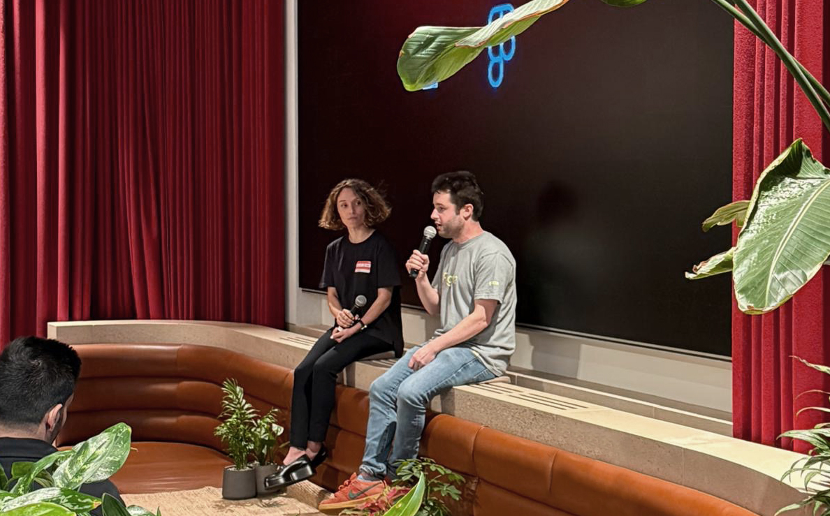 Figma CEO Dylan Field speaks with a colleague during a talk at the Leadership Launch event, seated on a stage with plants and a large screen in the background.