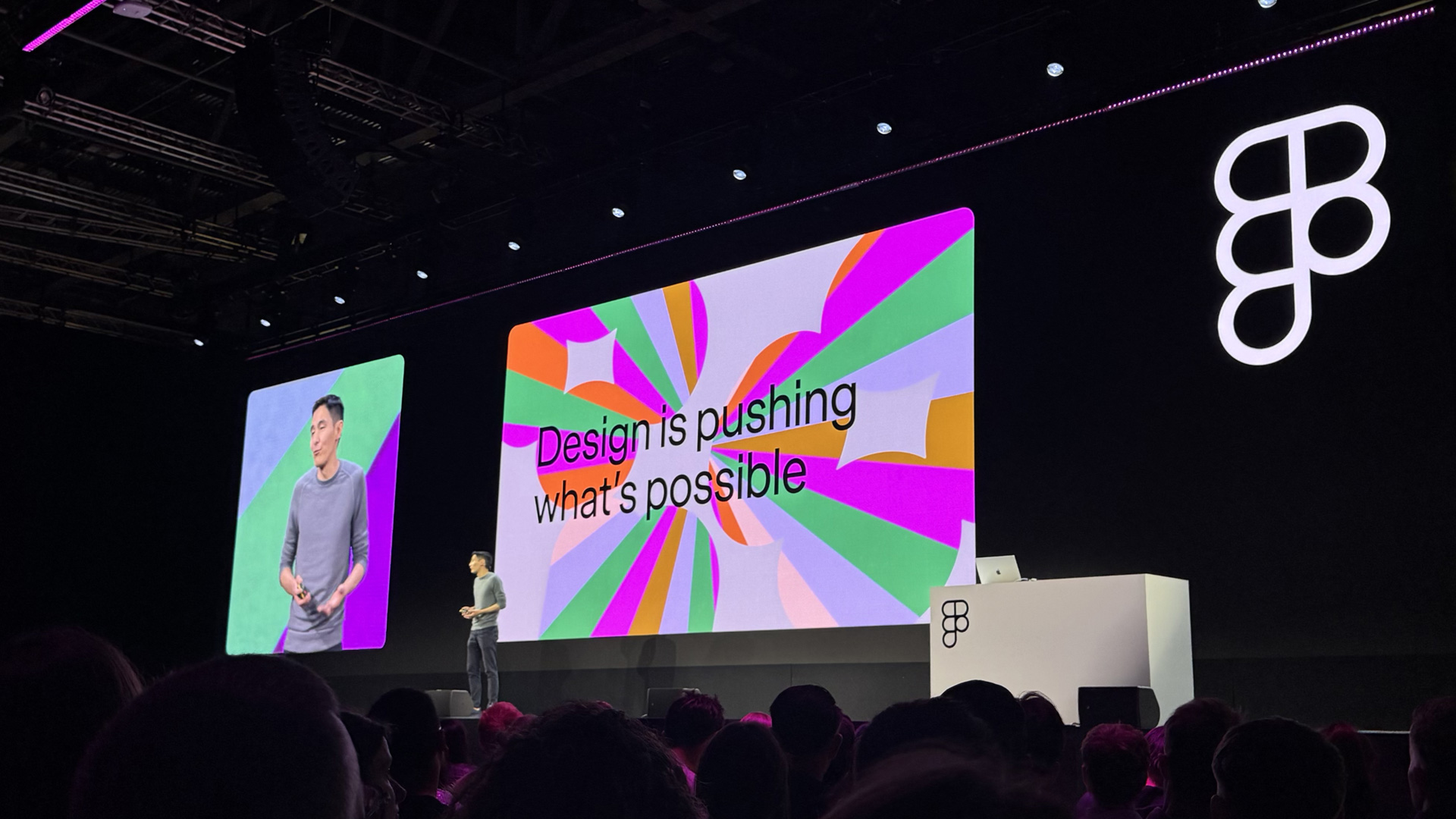 Yuhki Yamashita presents on stage at Figma Config 2025, unveiling new Figma products in front of a large audience. The screen behind shows the phrase "Design is pushing what’s possible" with colorful abstract graphics and the Figma logo.