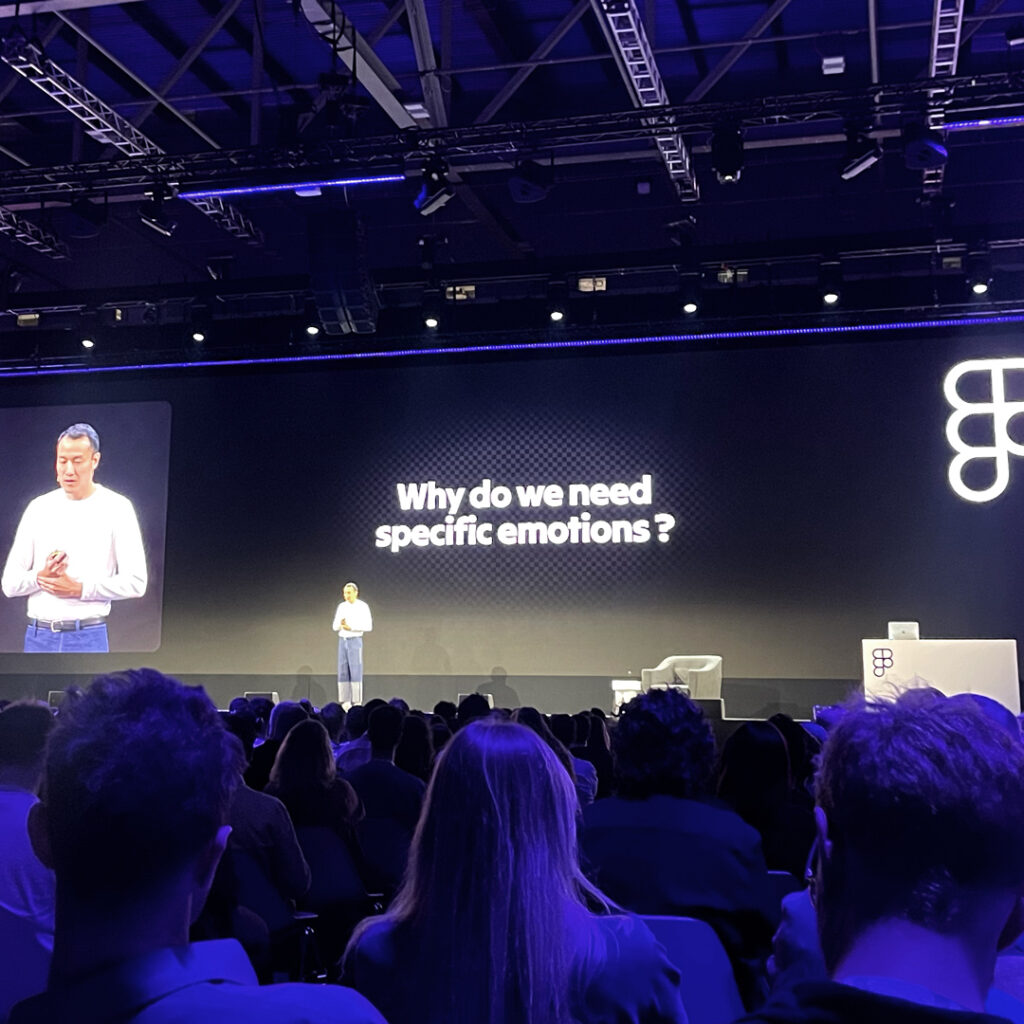 Ningfei Ou, a content designer at Google spresentin on a big stage behind him a screen showing "Why do we need basic emotions?"