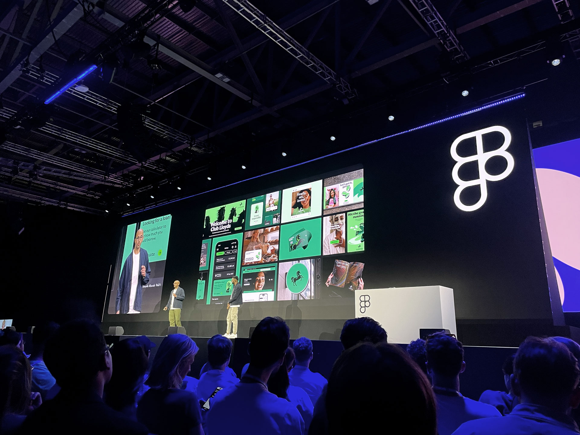 Vishal Kapoor and Kishan Koriya from Lloyds Banking Group standing on a big stage behind them a big screen showing the new colorful branding from Lloyd's