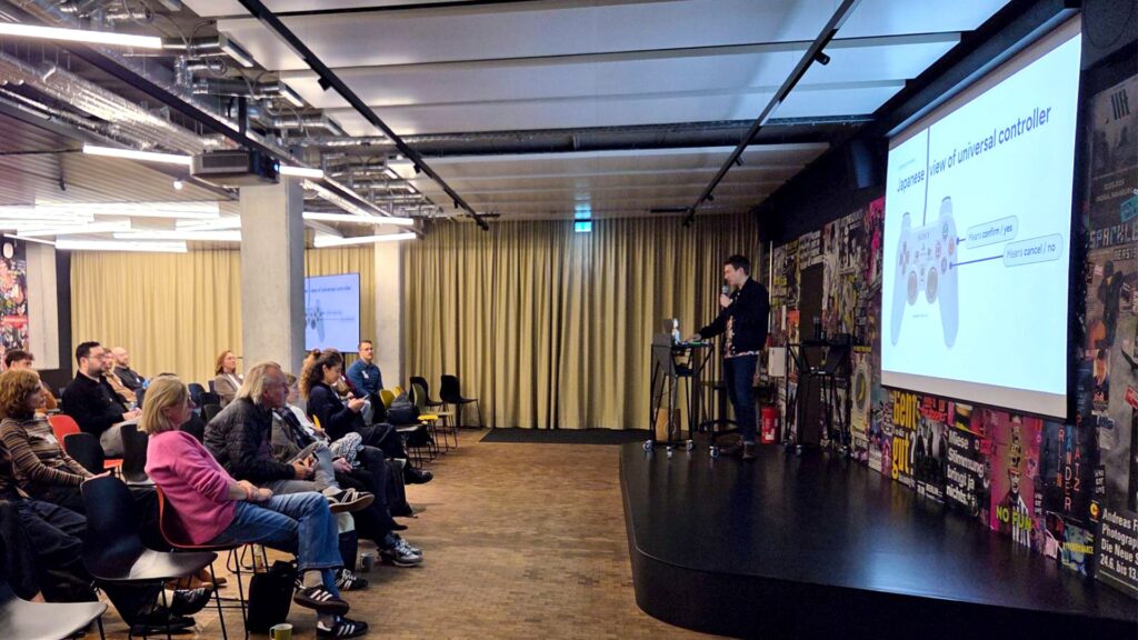 Speaker Guillaume Vaslin from Ennostudio explains cultural UX differences using a game controller at World Usability Day.