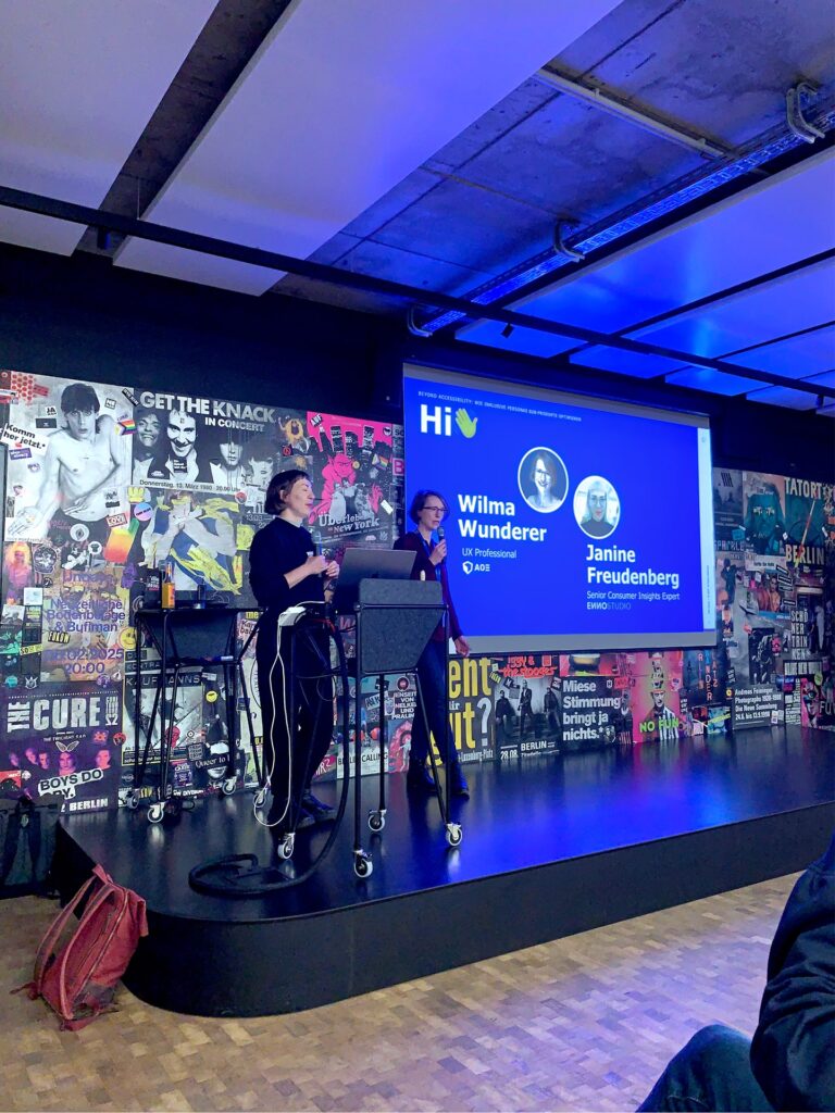 Speakerinnen Janine und Wilma stehen auf einer Bühne beim World Usability Day und stellen sich vor.